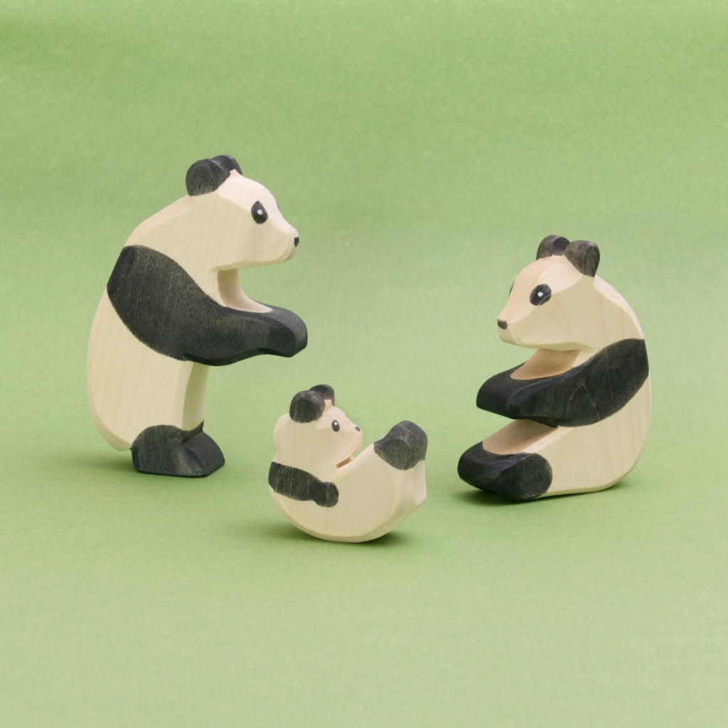 Zu sehen ist eine Panda Familie, alle drei Holzfiguren sind von Ostheimer und werden in Handarbeit in Deutschland gefertigt. Der größte Panda steht links, ein weiterer sitzt rechts und sie schauen zu dem Pandababy, was in der Mitte zwischen ihnen liegt.