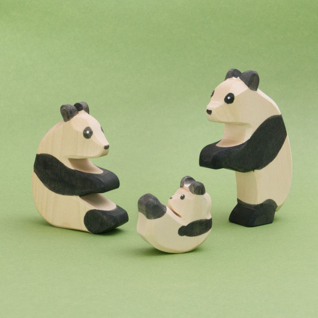 Die Panda Familie die hier zu sehen ist, zeigt drei Pandabären aus Holz in schwarzweiß. Ein Panda sitzt links, ein Panda steht rechts und tanzt, ein Pandabärbaby purzelt herum. Die Spielfiguren von Ostheimer sind handbemalt und aus Buchenholz gefertigt.