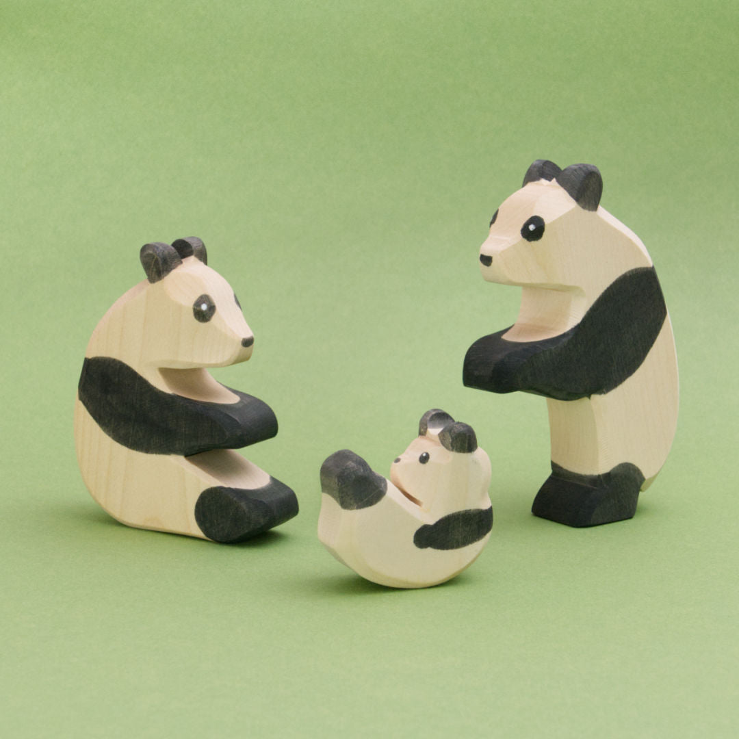 Die Panda Familie die hier zu sehen ist, zeigt drei Pandabären aus Holz in schwarzweiß. Ein Panda sitzt links, ein Panda steht rechts und tanzt, ein Pandabärbaby purzelt herum. Die Spielfiguren von Ostheimer sind handbemalt und aus Buchenholz gefertigt.