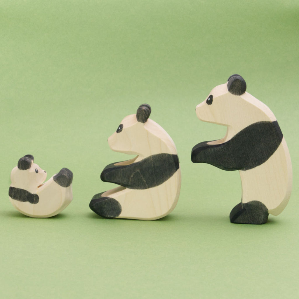 Die Pandafamilie die hier zu sehen ist, zeigt drei Pandabären aus Holz in schwarz-weiß. Die Pandas sind in einer Reihe von klein nach groß zu sehen. Links ist das Pandababy zu dem sitzenden Panda gedreht, der sitzende Panda und der tanzende Panda wenden sich dem Panda Baby zu.