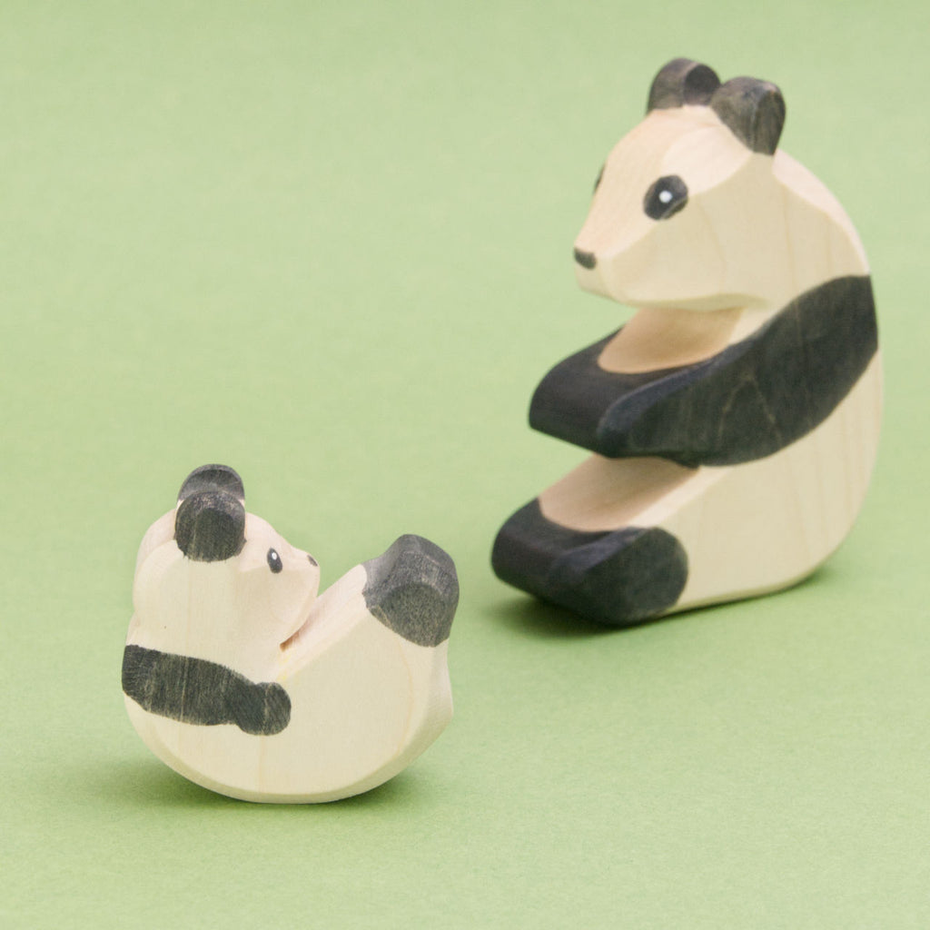 Hier sind zwei holz Panda Bären zusehen, wobei das PandaBaby das zu dem sitzenden Panda hinaufschaut. Die handgemachten Holzsbären für Jungs und Mädchen haben schwarze Ohren. Durch die sichtbare Buchenholz Maserung ist erkennbar, es handelt sich um deutsche, ungiftige Holzfiguren.