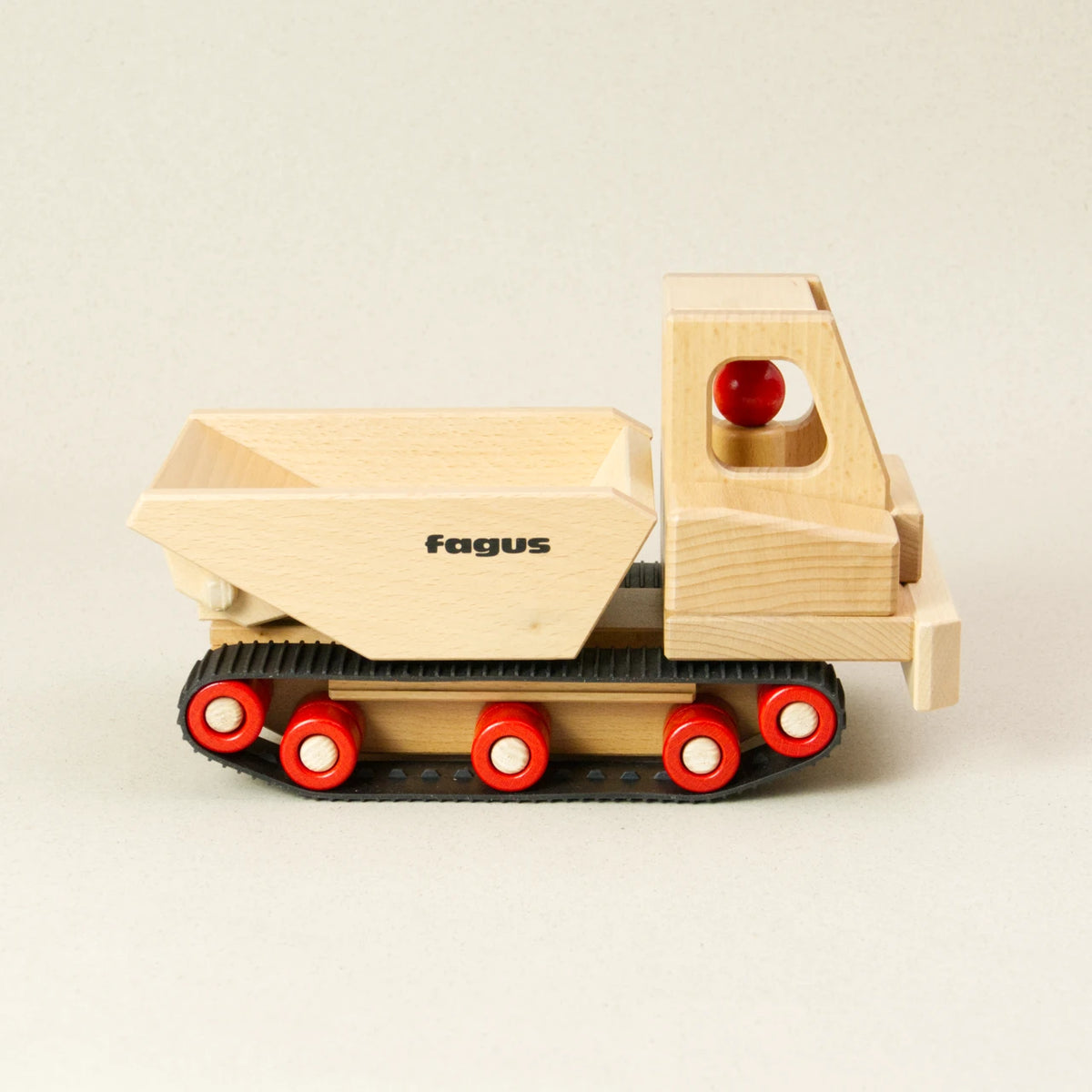 Das fagus Holzauto Raupen Dumper ist aus naturbelassenem Buchenholz und hat eine kantige Lademulde. Es fährt auf schwarzen Gummiketten mit roten Rollen. In der Fahrerkabine sitzt eine Holzfigur.