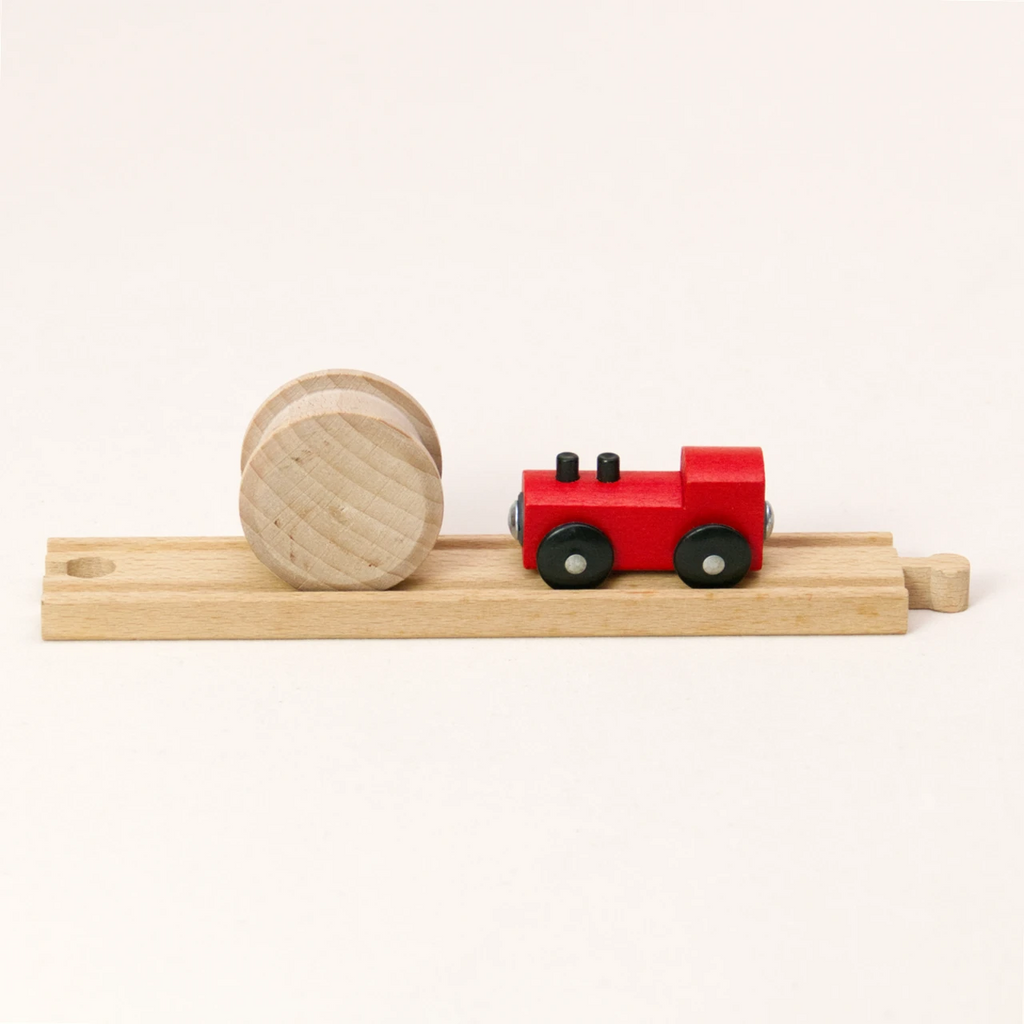 Zu sehen sind die Holzwalze Rolli von Yamba und eine rote Spielzeug-Lokomotive mit schwarzen Rädern auf einer geraden Holzschiene (BRIO®, IKEA®, Eichhorn®, Hape® usw.). Der Rolli hat die Form eines Zylinders und passt mit seinen Kufen in die Eisenbahnschiene. Er besteht aus naturbelassener Schweizer Buche und ist aus einem Stück gefertigt.