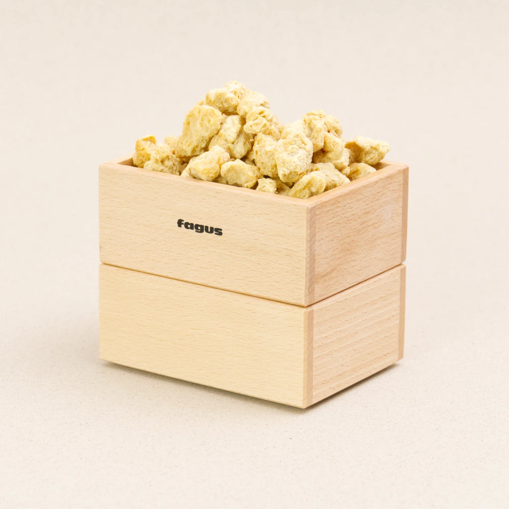 Zwei Stapelboxen von fagus aus naturlackiertem Buchenholz stehen aufeinander, die obere ist mit Schüttgut gefüllt. Sie haben das fagus Logo auf der längeren Seite.