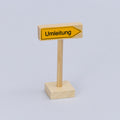 Spielzeug Umleitungsschild von der Marke Beck aus Holz. Auf einem länglichen Quader ist ein gelber Pfeil, der nach rechts zeigt und den schwarze Schriftzug Umleitung trägt.