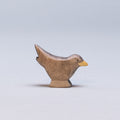 Eine Amsel von Holzviecherl mit einem orangenem Schnabel und dunklem Gefieder, hat einen nach oben hin gestreckten Schwanz.