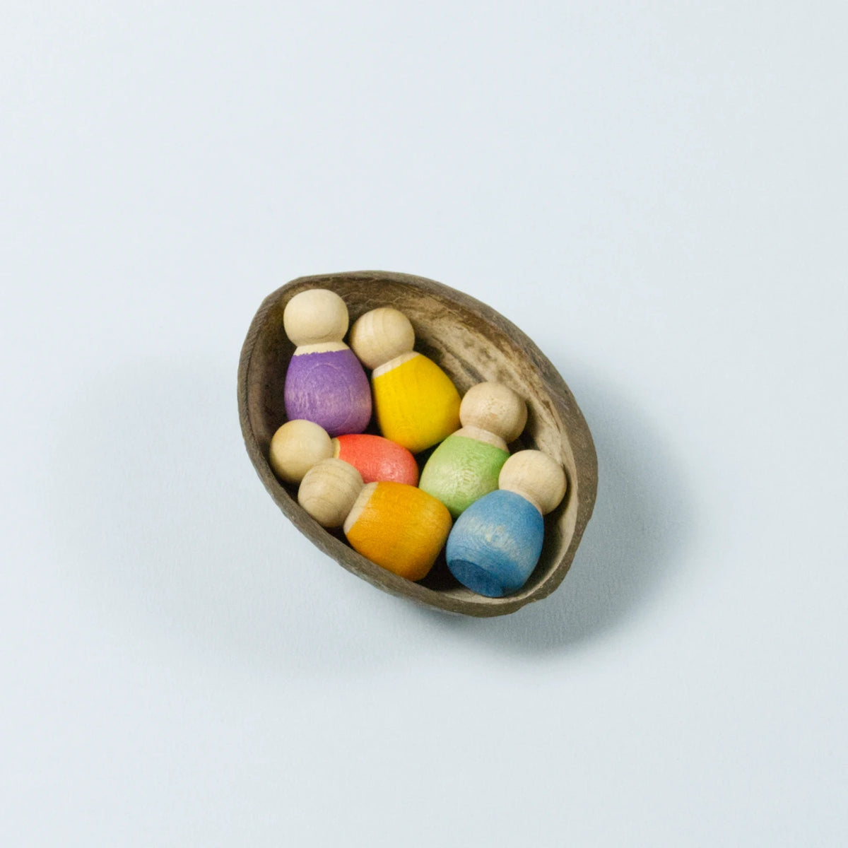 sechs kleine Babyholzfiguren in verschiedenen Farben in einer halben Kokosnussschale liegend.