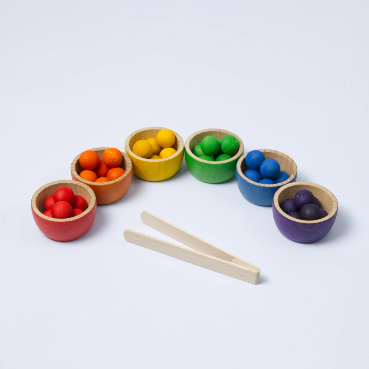 6 Holzbecher in welche je kleine Kugeln der passenden Farbe vom Becher einsortiert sind. Davor eine Holzzange.