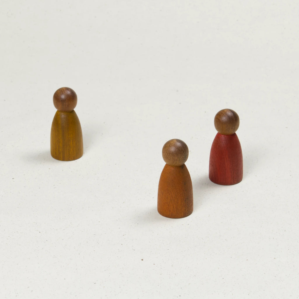 Drei gleichförmige Holzfiguren mit dunklerer Hautfarbe und Körpern in Gelb, Orange und Rot.