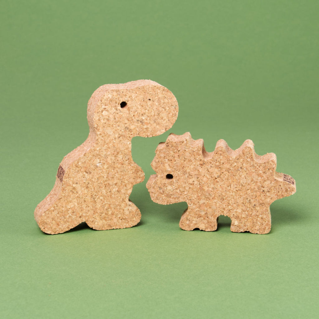 Das Dino Set 2 von Korxx, bestehend aus dem rechten Dino mit stacheligem Rücken und Kopf und linken Dino mit kleinem, aufrecht stehenden Körper. Beide schauen sich gegenseitig zur Bildmitte hin an und sind aus Kork gefertigt.