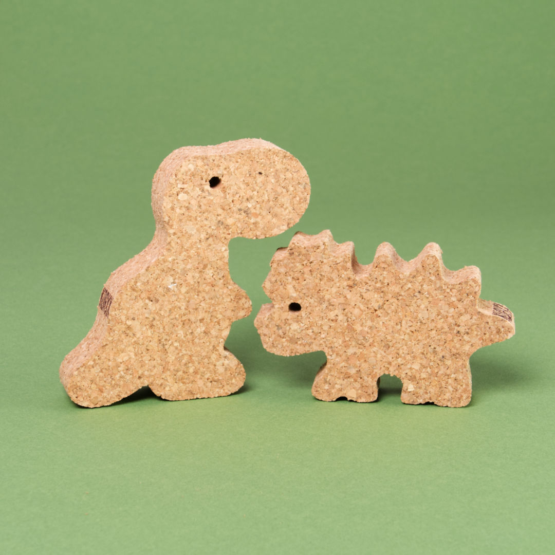 Das Dino Set 2 von Korxx, bestehend aus dem rechten Dino mit stacheligem Rücken und Kopf und linken Dino mit kleinem, aufrecht stehenden Körper. Beide schauen sich gegenseitig zur Bildmitte hin an und sind aus Kork gefertigt.