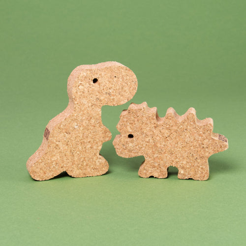 Das Dino Set 2 von Korxx, bestehend aus dem rechten Dino mit stacheligem Rücken und Kopf und linken Dino mit kleinem, aufrecht stehenden Körper. Beide schauen sich gegenseitig zur Bildmitte hin an und sind aus Kork gefertigt.