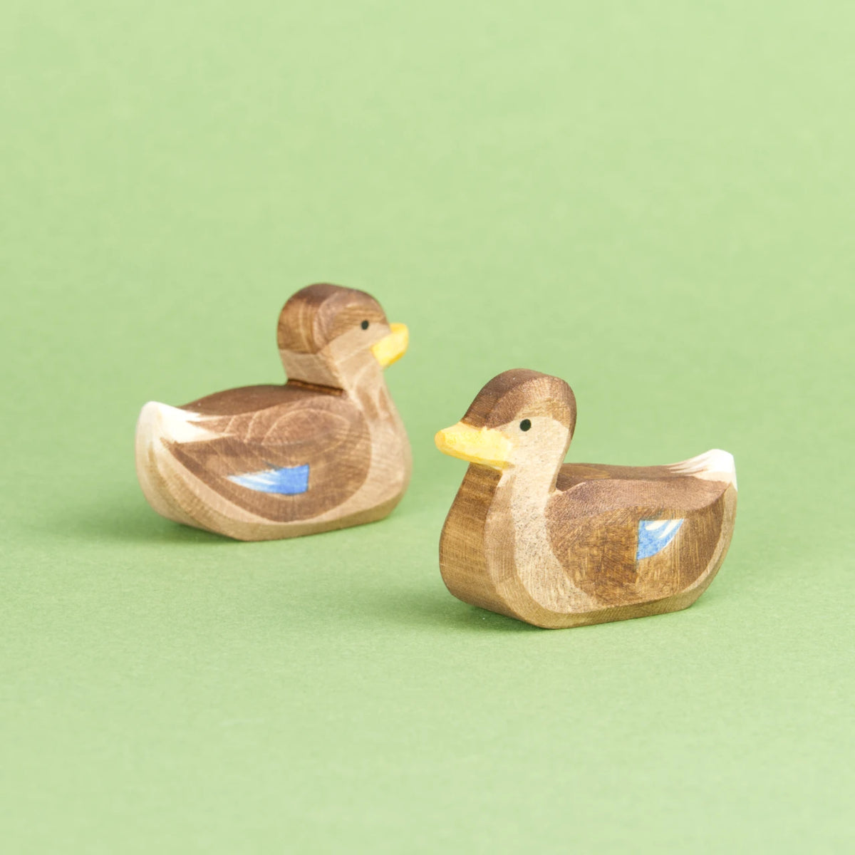 Zwei schwimmende Enten von Ostheimer aus Naturholz gefertigt, haben braunes Gefieder mit blauen und weißen Farbdetails, einen orangenen Schnabel und ein weißes Schwanzende. Beide schauen aneinander vorbei. Die Rechte nach vorne links und die Rechte nach hinten rechts.