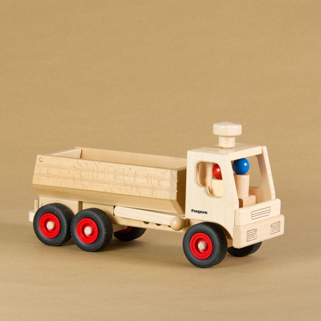 Muldenkipper-LKW von fagus aus naturlackiertem Buchenholz mit schwarzen Vollgummireifen und roten Radkappen. In der Fahrerkabine sitzen zwei Figuren, auf dem Dach ist ein Lenkknopf.