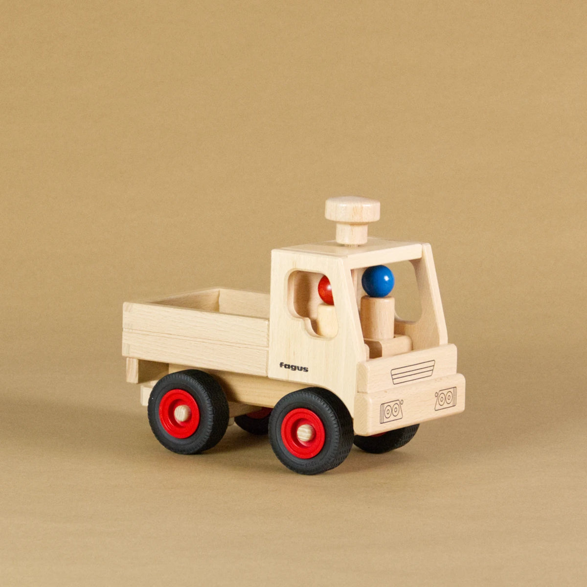 Unimog von fagus aus naturlackiertem Buchenholz, mit schwarzen Vollgummireifen und roten Radkappen. In der Fahrerkabine sitzen zwei Figuren, auf dem Dach ist ein Lenkknopf.