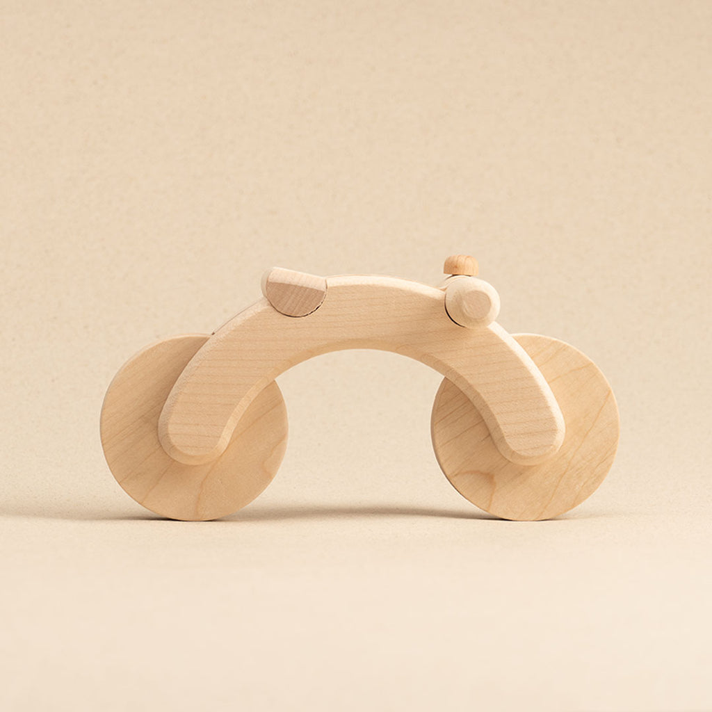 Seitenansicht eines in naturfarben gehaltenen Fahrrad aus PEFC-zertifiziertem Buchenholz mit zwei Rädern und einem Lenker mit linksseitiger Klingel und Sattel. Die Räder sind rollbar.