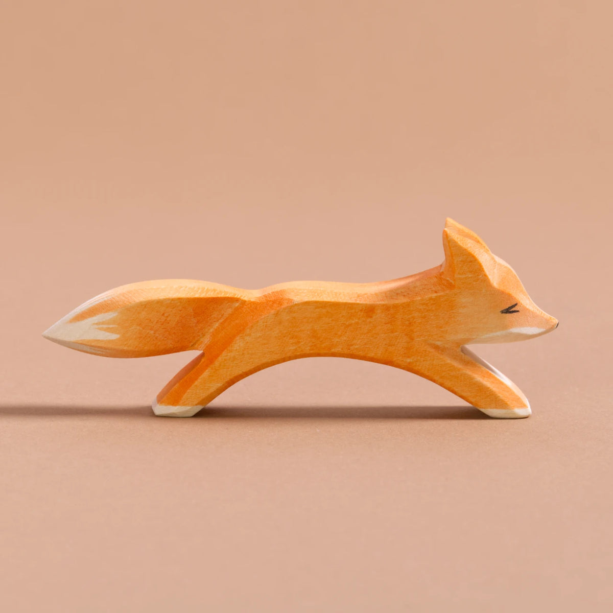 Ein grosser Fuchs ist in laufender Position, hat orangenes Fell, einen Schwanz mit weißer Spitze und weißes Bauchfell. Es schaut nach rechts.