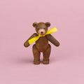 ein kleiner Teddybär aus dunklem Holz mit gelber Schleife um den Hals, Beine und Arme sind beweglich , er ist in einer stehenden Position zu sehen, er hat eine hellere Schnauze und seine Augen und Nase sind schwarz , sein Mund lächelt
