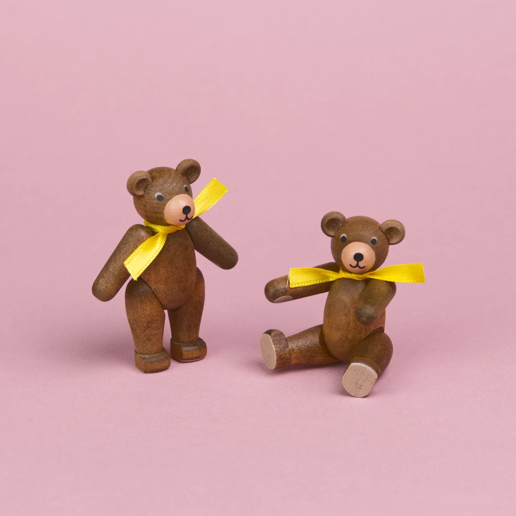 Zwei kleine Teddybären aus dunklem Holz mit gelben Schleifen um den Hals, Beine und Arme sind beweglich , einer ist in einer stehenden Position zu sehen der andere sitztund zeigt seine hellen Pfoten, beide haben eine hellere Schnauze und schwarze Augen und Nasen