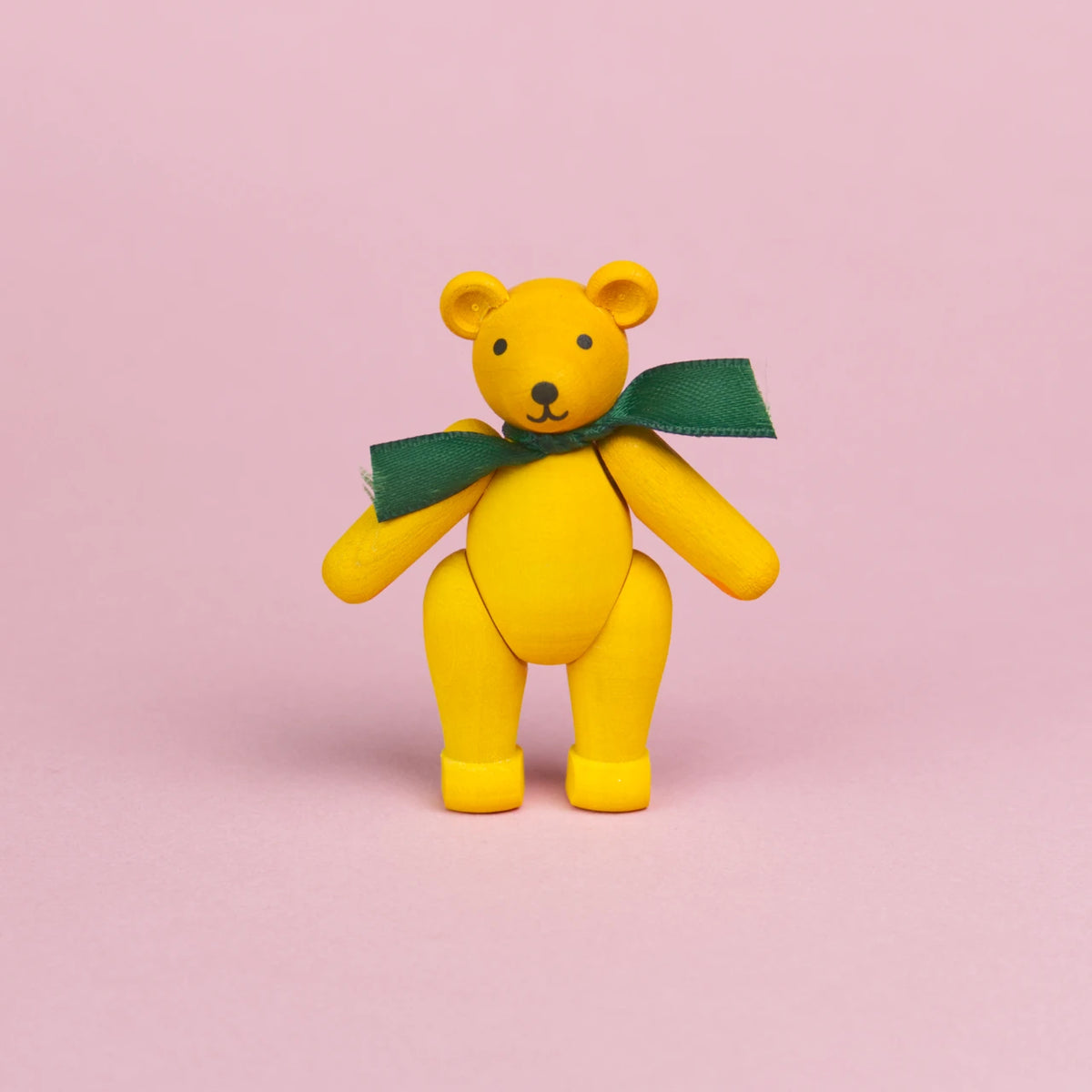 ein kleiner Teddybär aus gelb bemaltem Holz mit grüner Schleife um den Hals, Beine und Arme sind beweglich und er ist in einer stehenden Position zu sehen, seine Augen und Nase sind schwarz und sein Mund lächelt