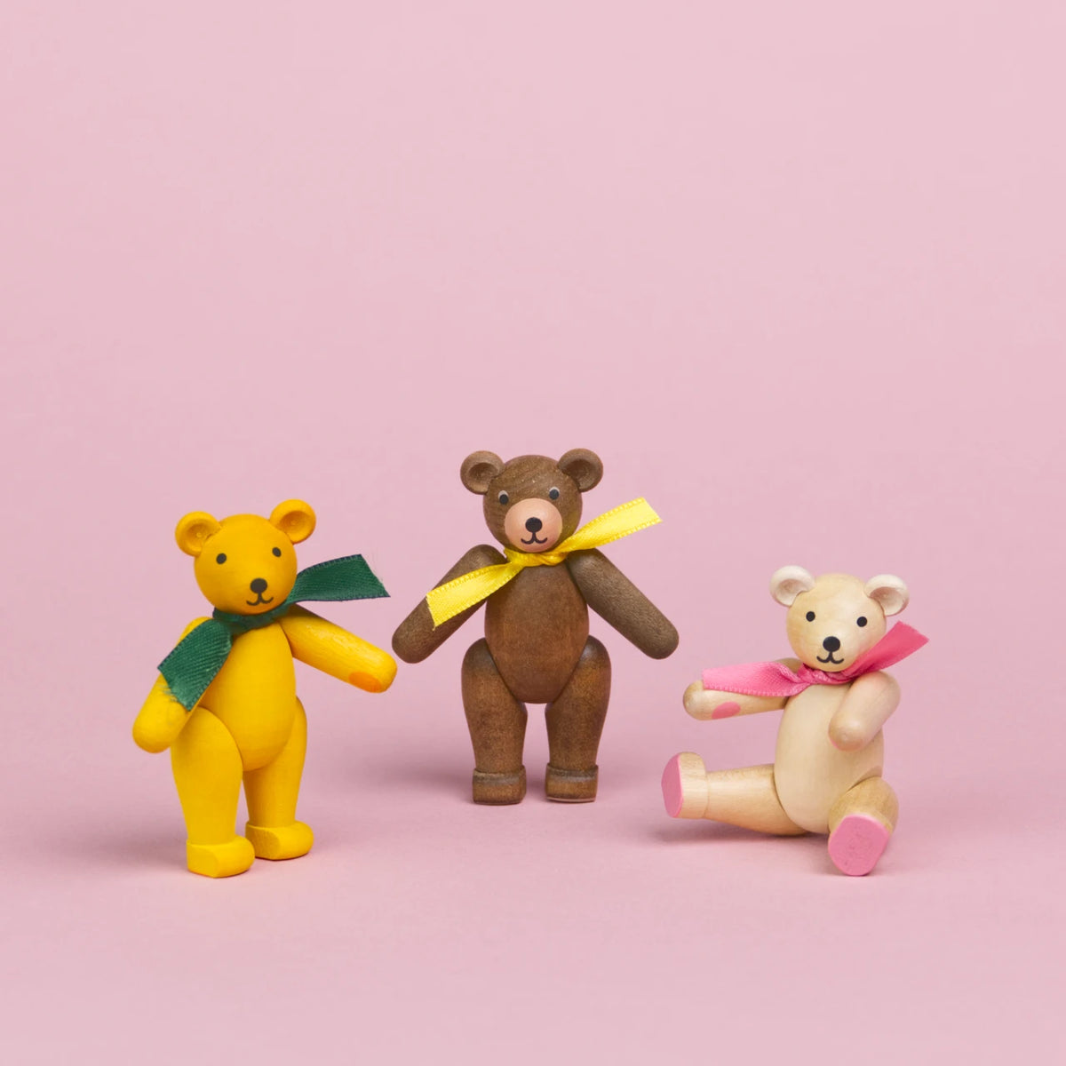Drei kleine Teddybären aus Holz , der erste ist gelb mit grüner Schleife, der zweite ist braun mit gelber Schleife, der dritte ist aus hellem Holz mit rosa Schleif, Beine und Arme sind beweglich , zwei sind in einer stehenden Position zu sehen der andere sitzt, sie haben schwarze Augen und Nasen