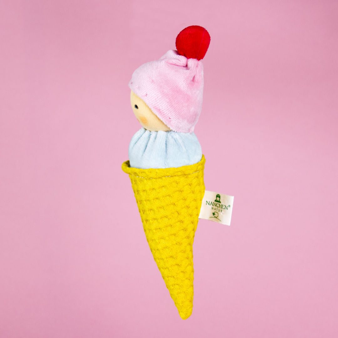 Seitenansicht des Plüschgreiflings "Eiswaffel" von Nanchen. Es trägt eine rosa Mütze mit rotem Bommel, ein hellblaues Oberteil und einen gelben Körper als Eiswaffel verkörpert.
