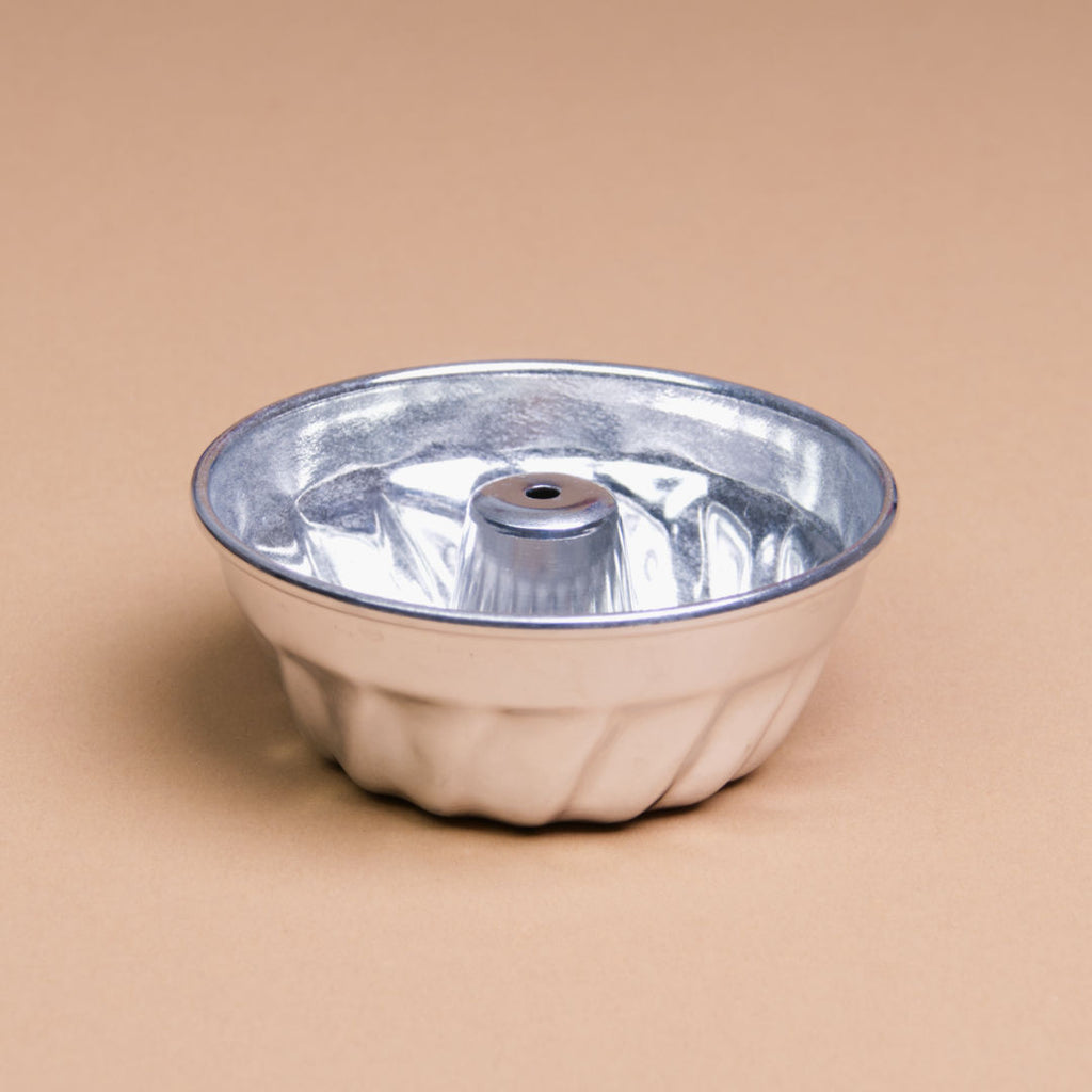 Eine Gugelhupfform aus Aluminium liegt mit der Öffnung nach oben da und hat einen Durchmesser von 10 cm.