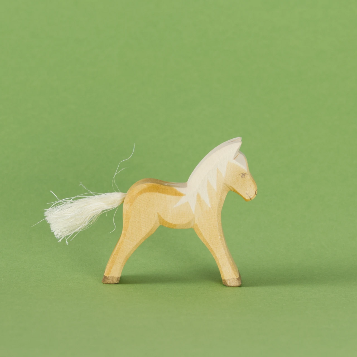 Ein Haflinger Fohlen von Ostheimer aus Naturholz gefertigt, hat weiße Mähne und einen weißen Schweif aus Naturhaar, braune Hufen sowie braune Farbdetails. Es schaut im Profil nach rechts.
