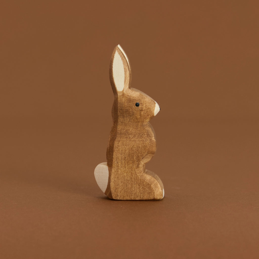 Ein brauner Hase mit nach oben zeigenden Ohren, von Ostheimer aus Naturholz gefertigt, schaut im Profil nach rechts, hat eine weiße Blume und Nasenspitze.