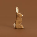Ein brauner Hase mit nach oben zeigenden Ohren, von Ostheimer aus Naturholz gefertigt, schaut im Profil nach rechts, hat eine weiße Blume und Nasenspitze.