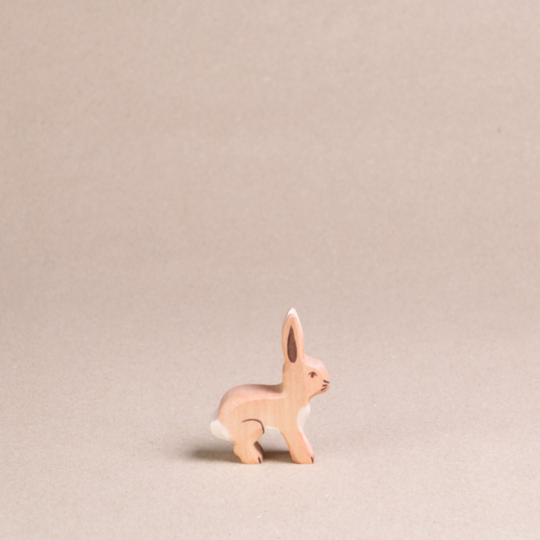 Ein Hase mit nach oben hin stehenden Ohren von Holztiger, hat hellbraunes Fell, einen weißen Schwanz sowie Bauchfell. Es schaut nach rechts.