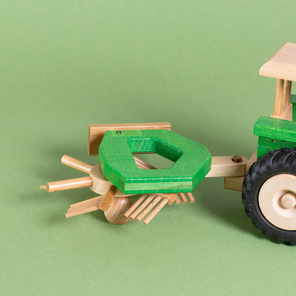 Ein grüner, an den Traktor angehängten Heuwender mit sich drehendem Rad.