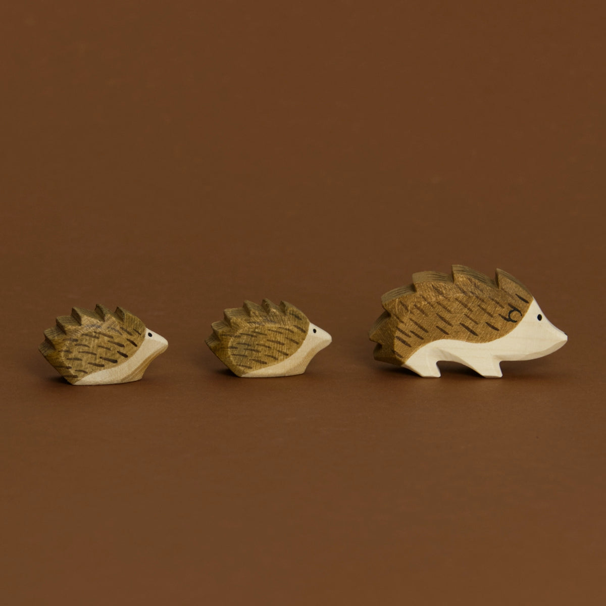 Eine Komposition von drei Igeln, aus Igel, Igel klein und Igel klein, im Profil nach rechts schauend, sind von Ostheimer aus Naturholz gefertigt. Alle haben braune Stacheln und helles Bauchfell. Beide kleinen Igel folgen dem Igel.