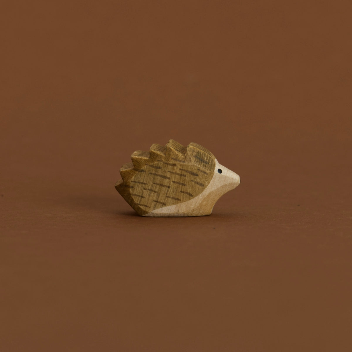 Ein kleiner Igel von Ostheimer aus Naturholz gefertigt, schaut im Profil nach rechts, hat dunkelbraune Stacheln und naturfarbenes Bauchfell.