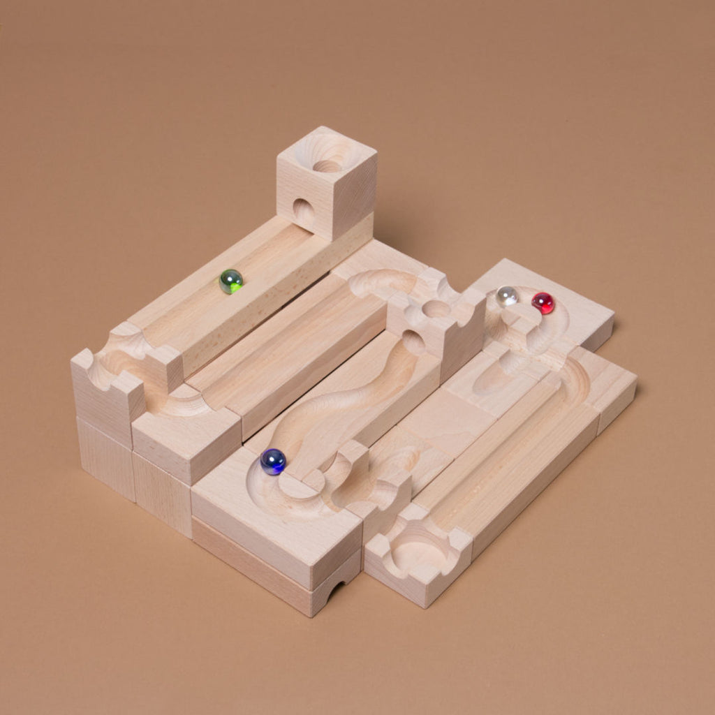 Das als Bahn aufgebaute Junior Starter Set von Cuboro aus Buche gefertigt mit vier Glasmurmeln in grün, rot, blau und durchsichtig, in der Bahn liegend.