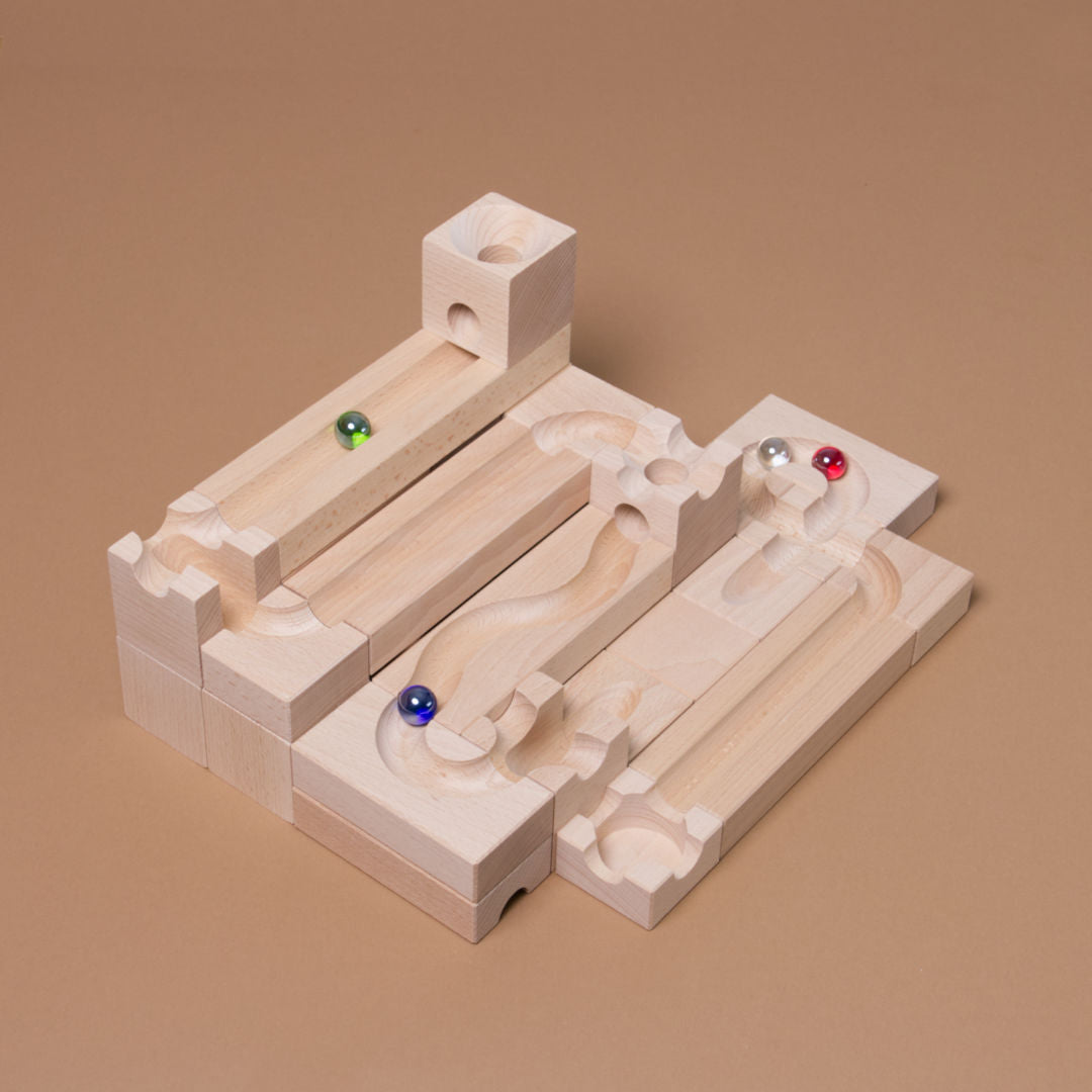 Das als Bahn aufgebaute Junior Starter Set von Cuboro aus Buche gefertigt mit vier Glasmurmeln in grün, rot, blau und durchsichtig, in der Bahn liegend.