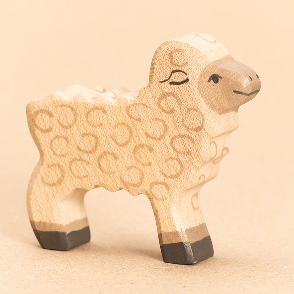 Ein im Profil nach rechts blickendes Lamm aus Holz mit beigem Fell, hellbraunem Kopf, sowie dunkelbraunen Hufen. Das Felltexturat wird durch kreisförmige Bemalung verdeutlicht.