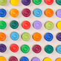 36 Regenbogen Blumen aus Holz von Grapat in 12 unterschiedlichen Farben. Dunkelblau, dunkellila, hellblau, pastelllila, grasgrün, hellgrün, dunkelgrün, dunkelrot, orange, rot, sonnengelb und senfgelb. Gemeinsam als Quadratischer Block aufgebaut. Ansicht von Oben. Alle sind farblich wild durchmischt angeordnet.