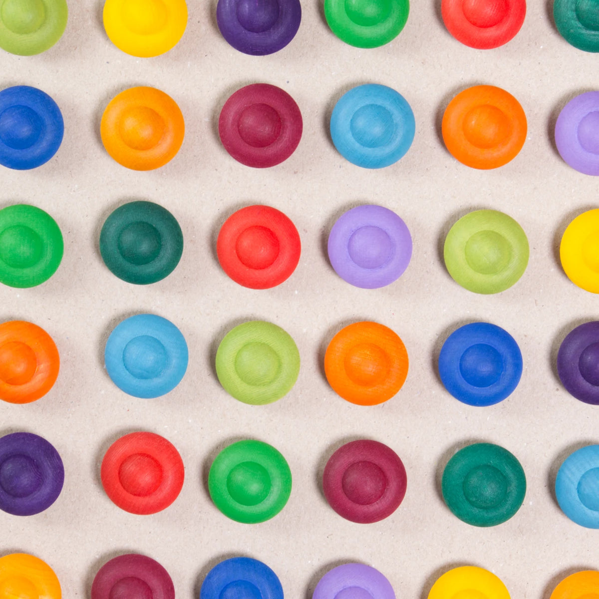 36 Regenbogen Blumen aus Holz von Grapat in 12 unterschiedlichen Farben. Dunkelblau, dunkellila, hellblau, pastelllila, grasgrün, hellgrün, dunkelgrün, dunkelrot, orange, rot, sonnengelb und senfgelb. Gemeinsam als Quadratischer Block aufgebaut. Ansicht von Oben. Alle sind farblich wild durchmischt angeordnet.