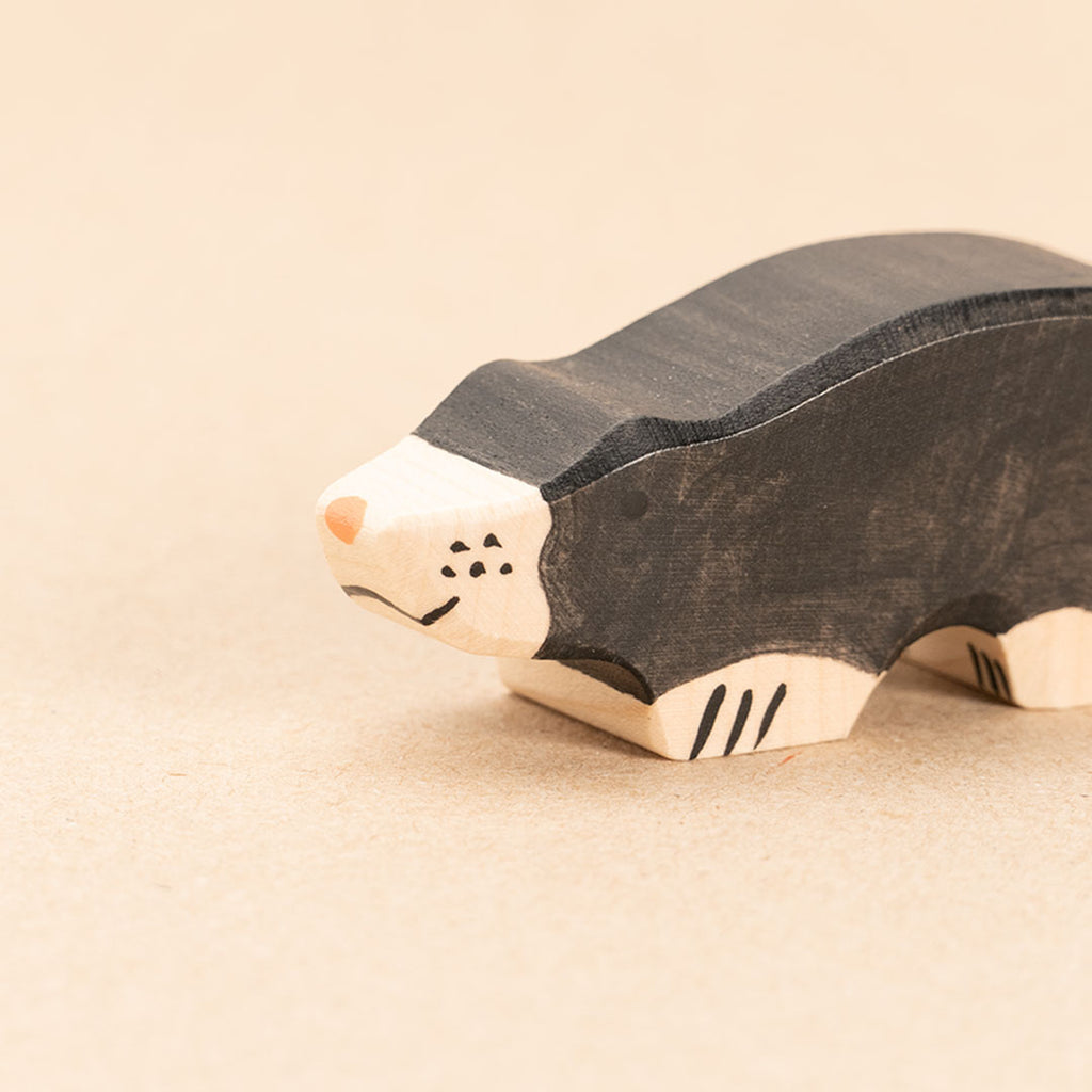 Die Nahaufnahme zeigt einen Maulwurf aus Holz mit schwarzer Haut und hellen Pfoten. Das Gesicht teilt sich in eine schwarze und helle Hälfte. Die helle Hälfte weist Bemalungen auf. Seine Nase ist hellrot. Das Hintere Teil ist nicht mehr sichtbar.
