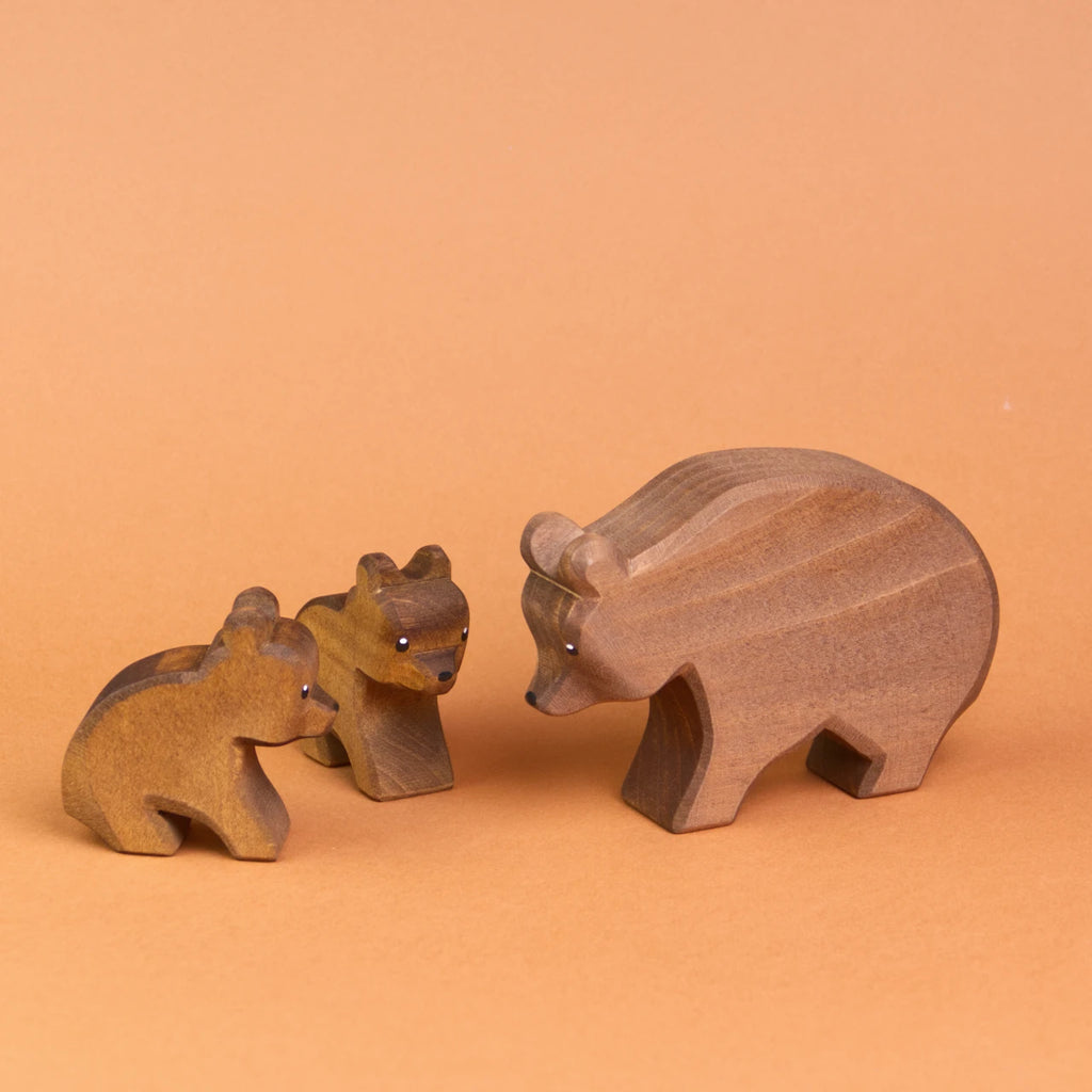 Drei Ostheimertiere Bären aus Holz. Es ist rechts ein großer Bär von der Seite zu sehen, der zu zwei kleinen Bären herunter schaut, die links von ihm sitzen. Der vordere, kleine Bär ist von der Seite zu sehen, der hintere kleine Bär schaut nach vorne rechts.