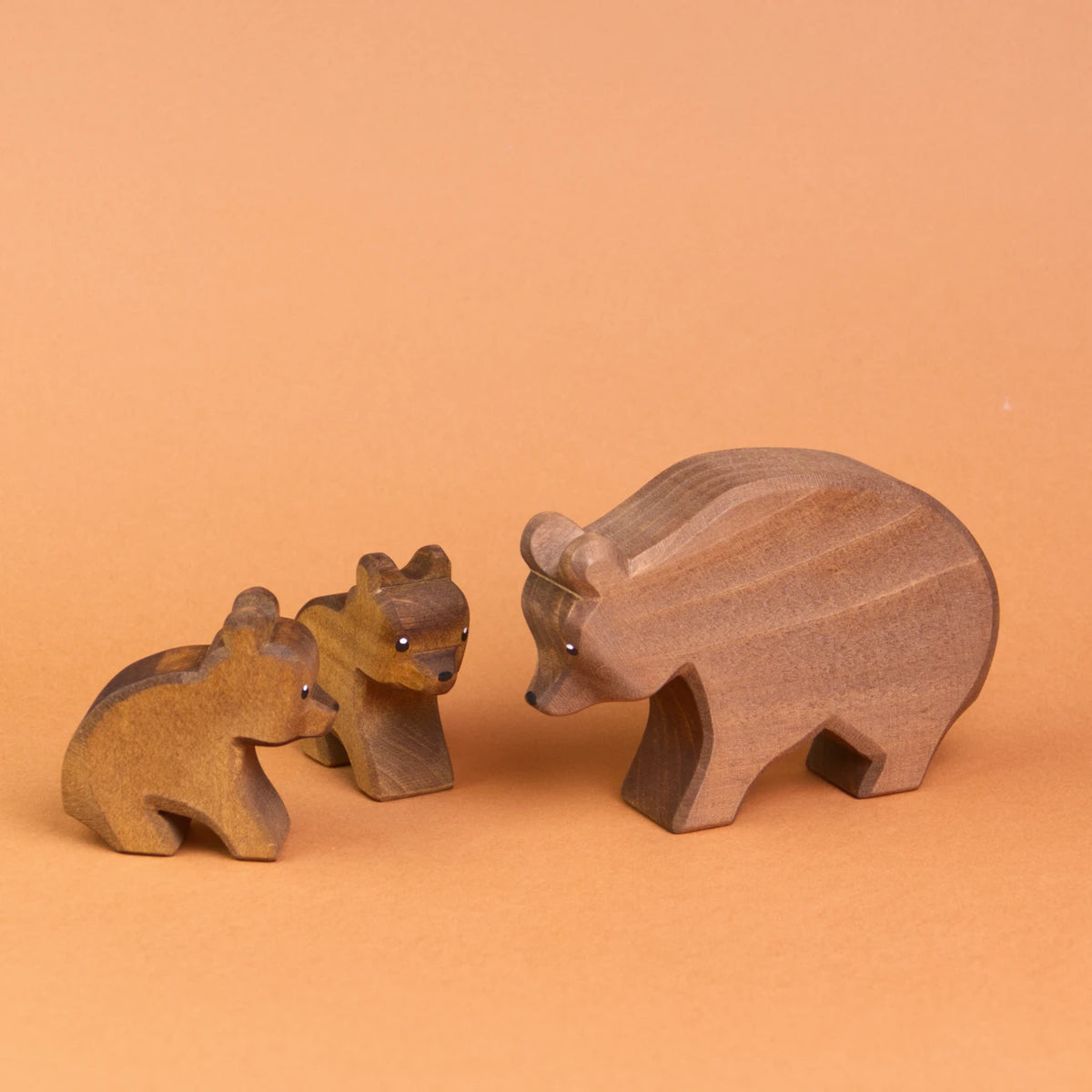 Drei Ostheimertiere Bären aus Holz. Es ist rechts ein großer Bär von der Seite zu sehen, der zu zwei kleinen Bären herunter schaut, die links von ihm sitzen. Der vordere, kleine Bär ist von der Seite zu sehen, der hintere kleine Bär schaut nach vorne rechts.