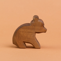 Ein kleiner, sitzender Bär aus Holz ist in der Seitenansicht zu sehen und schaut nach rechts. Er hat dunkelbraunes Fell und runde, hochstehende Ohren. Er ist von der Marke Ostheimer.