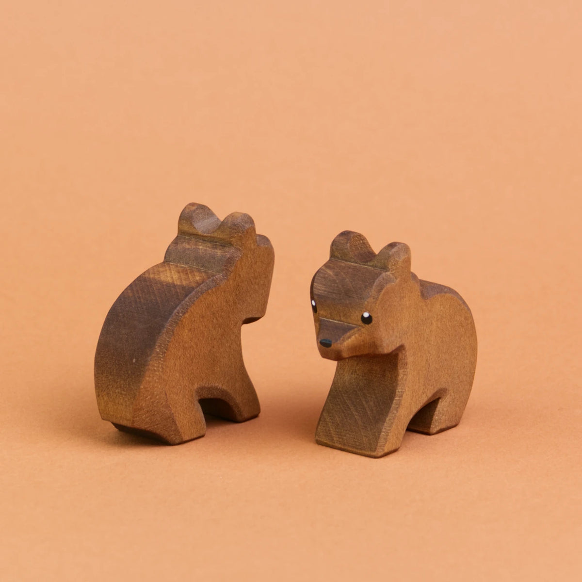 Zwei kleine Bären aus Holz sind schräg nebeneinander sitzend zu sehen. Der recht Bär schaut nach vorne links, der linke Bär schaut nach hinten rechts und ist nur von hinten zu sehen.