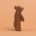 Ein kleiner Bär aus Holz ist stehend in der Seitenansicht zu sehen und schaut nach rechts, oben. Er hat dunkelbraunes Fell und große, runde Ohren. Er ist von der Marke Ostheimer.