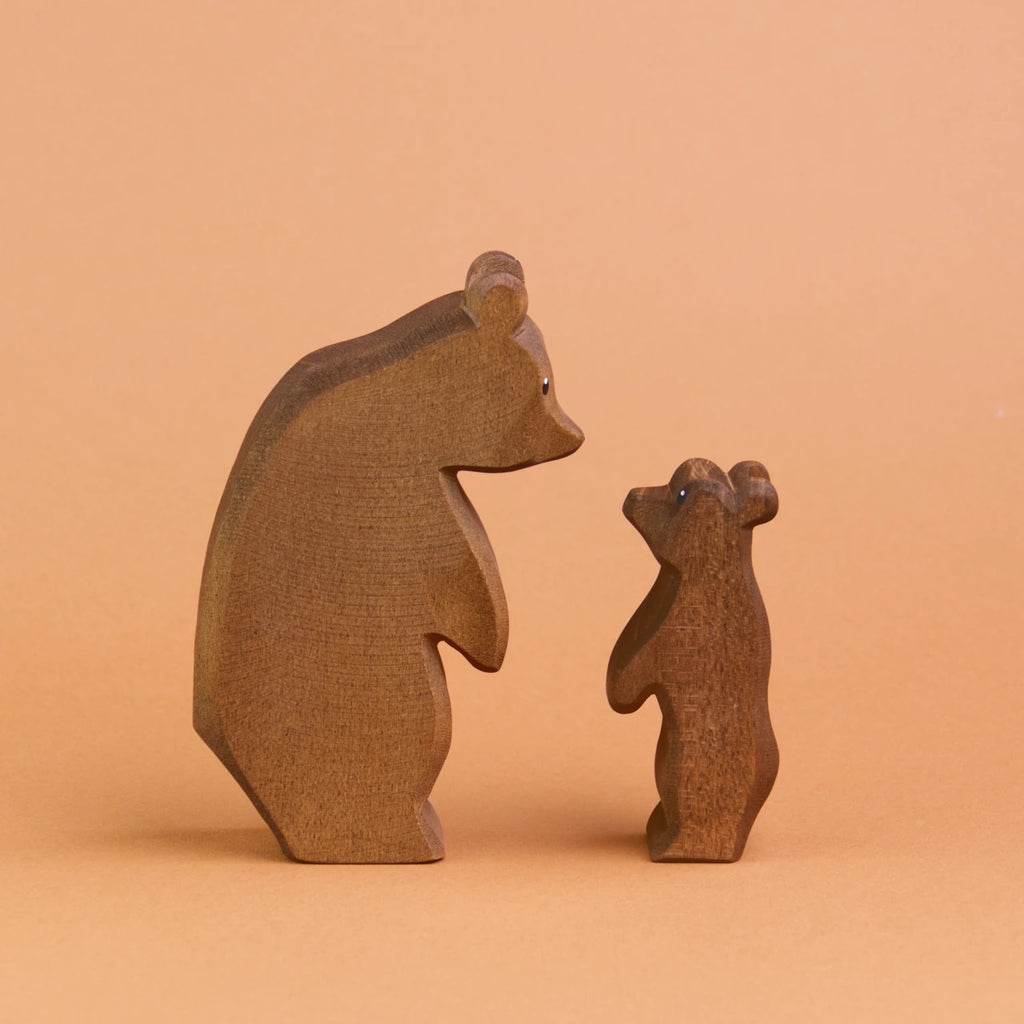 Es sind zwei Bären aus Holz in der Seitenansicht zu sehen. Ein großer stehender Bär steht links und schaut herunter zu einem kleinen stehenden Bär rechts, der nach oben schaut.