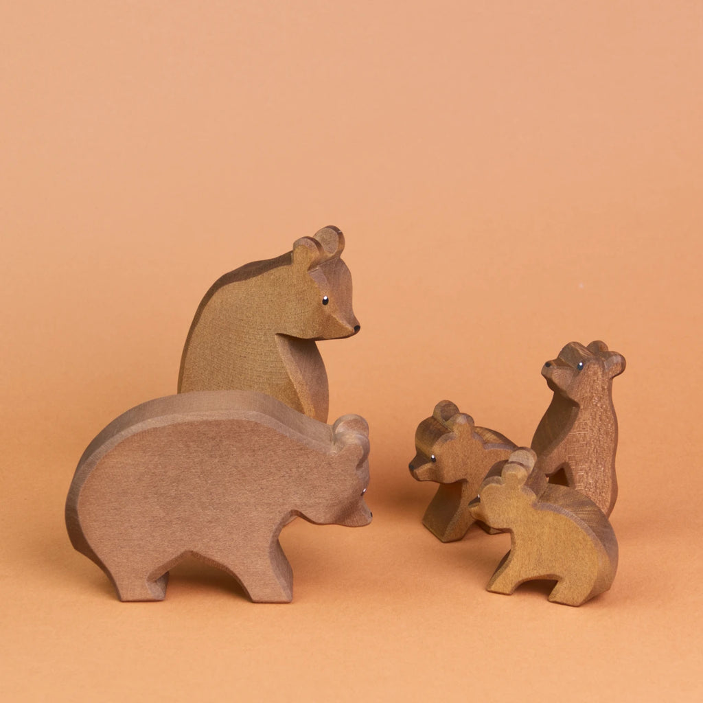 Es ist eine Bärenfamilie aus Holz zu sehen, die sich anschauen. Ganz vorne steht ein großer Bär, der zu zwei kleinen, sitzenden Bären herüber schaut, die ebenfalls zu dem großen Bär schauen. Weiter hinten, hinter dem großen Bär ist ein stehender, großer Bär zu sehen, der zu einem kleinen stehenden Bär herunter schaut, der etwas weiter hinter den zwei sitzenden Bären steht und hoch schaut.