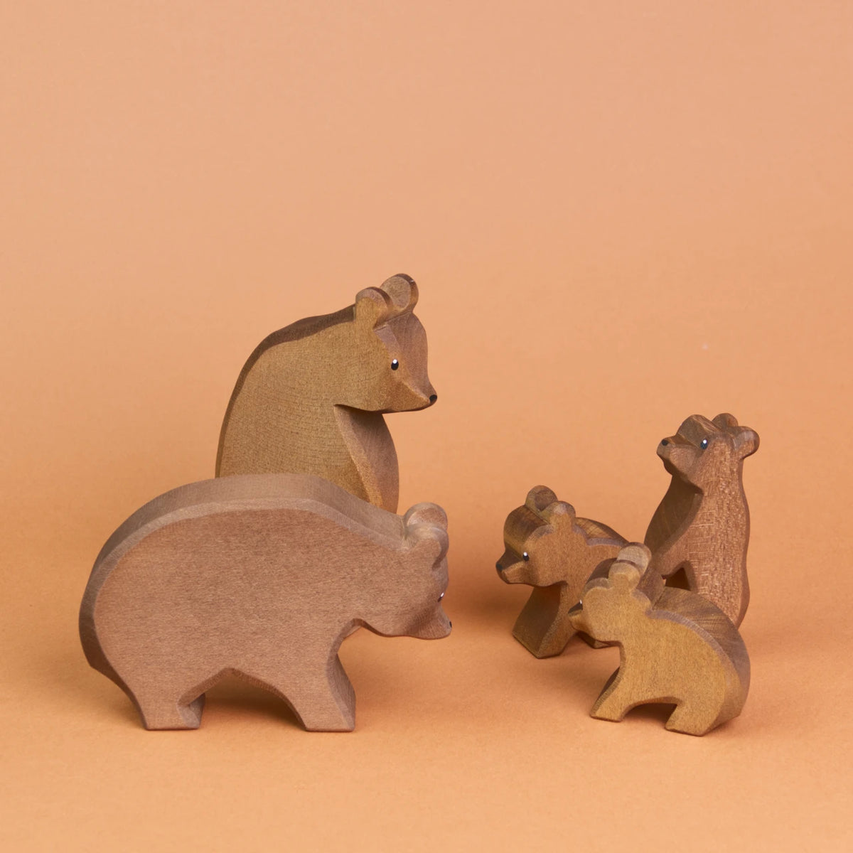 Es ist eine Bärenfamilie aus Holz zu sehen, die sich anschauen. Ganz vorne steht ein großer Bär, der zu zwei kleinen, sitzenden Bären herüber schaut, die ebenfalls zu dem großen Bär schauen. Weiter hinten, hinter dem großen Bär ist ein stehender, großer Bär zu sehen, der zu einem kleinen stehenden Bär herunter schaut, der etwas weiter hinter den zwei sitzenden Bären steht und hoch schaut.