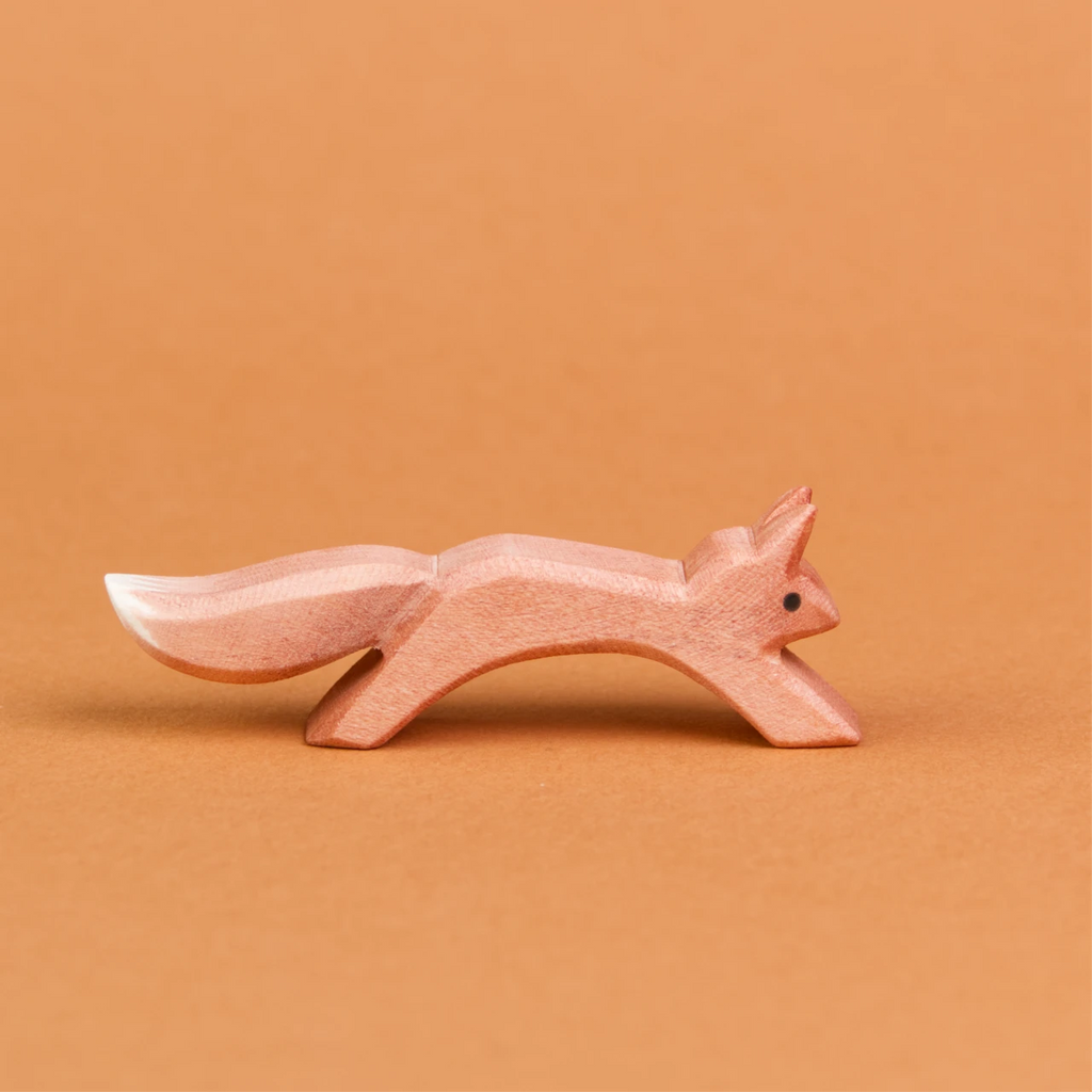 Es ist ein springendes Eichhörnchen aus Holz in der Seitenansicht zu sehen, welches nach rechts schaut. Es hat ein rötlich, braunes Fell, welches am Ende seines Schwanzes weiß gefärbt ist. Seine Ohren stehen nach oben und es ist von der Marke Ostheimer.
