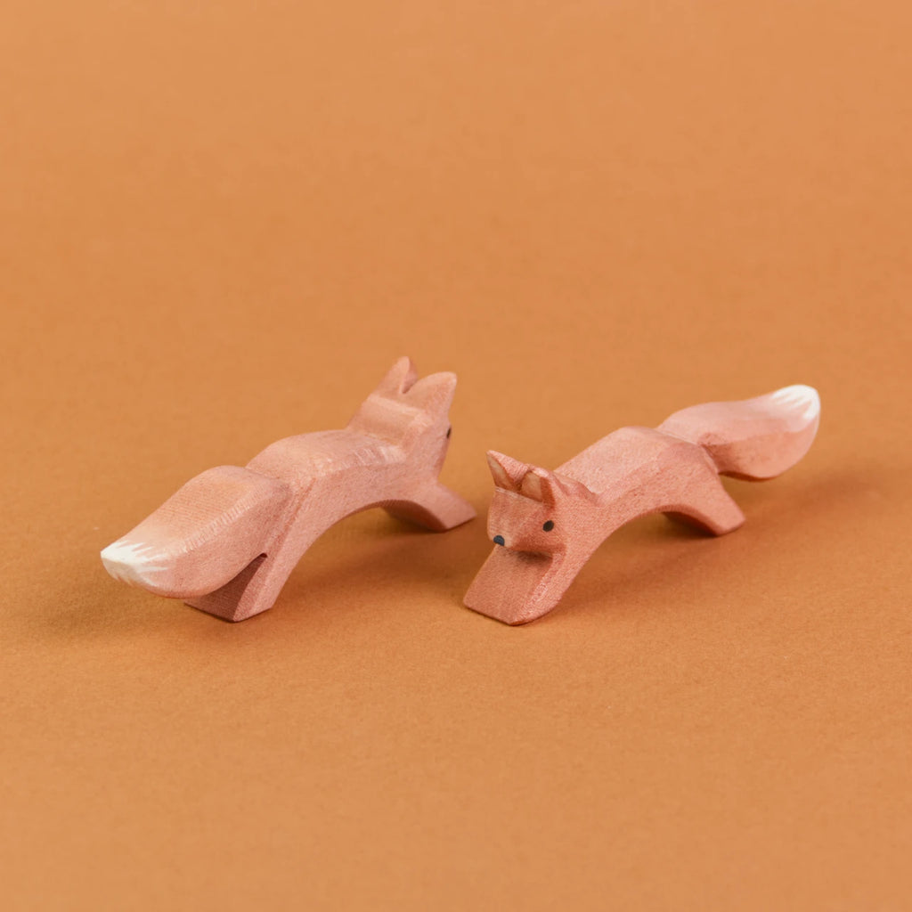 Es sind zwei springende Eichhörnchen aus Holz zu sehen, die parallel, nebeneinander stehen. Das linke Eichhörnchen schaut nach hinten rechts, das rechte Eichhörnchen schaut nach vorne links.